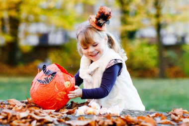 Cadılar Bayramı 'nda cadı kılığına girmiş küçük bir kız. Mutlu çocuk dışarıda, turuncu komik şapkası ve tatlı lanetli balkabağı çantasıyla. Ekim 'de aile festivali sezonu. Açık hava aktivitesi.