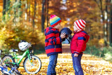 İki küçük çocuk, sonbahar ormanında en iyi arkadaşlar. Ağabeyim, doğada güneşli bir sonbahar gününde bisiklete binmeden önce küçük çocuğun kaskını takmasına yardım ediyor. Güvenlik, spor, çocuk konseptiyle eğlence..