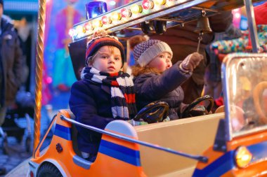 Sevimli küçük erkek ve kız, Noel funfair veya pazar, açık havada bir atlıkarınca üzerinde kardeşler. Mutlu çocuklar, arkadaşlar eğleniyor. Bir çocuğa seçici bir odaklanma. Tatil, çocuklar, yaşam tarzı kavramı.