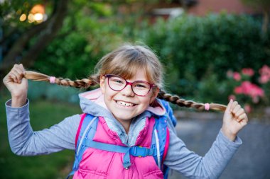 Gözlüklü ve sırt çantalı mutlu bir ilkokul öğrencisi okula giderken yolda yürüyor. Gülümseyen öğrenci okula, eğitime ve çocukluk yaşam tarzı konseptine hazır..