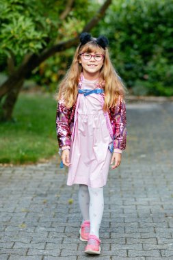 Gözlüklü ve sırt çantalı mutlu bir ilkokul öğrencisi okula giderken yolda yürüyor. Gülümseyen öğrenci okula, eğitime ve çocukluk yaşam tarzı konseptine hazır..