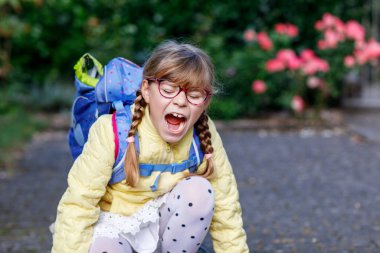 Gözlüklü ve sırt çantalı mutlu bir ilkokul öğrencisi okula giderken yolda yürüyor. Gülümseyen öğrenci okula, eğitime ve çocukluk yaşam tarzı konseptine hazır..