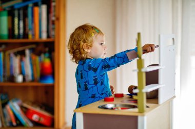 Oyuncak mutfağıyla oynayan sevimli küçük bir kız. Mutlu sağlıklı bir bebek. Rol yapma oyunuyla eğleniyor, evde veya çocuk odasında çömlek çaydanlığıyla oynuyor. Oyuncağı olan aktif bir çocuk
