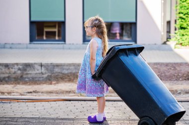 Gözlüklü küçük anaokulu kızı çöp tenekesi alıyor. Çocuk atık ayıklamayı öğreniyor. Çevre kavramı