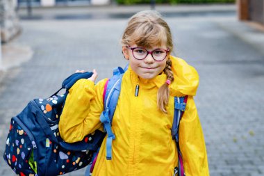 Gözlüklü ve sırt çantalı mutlu bir ilkokul öğrencisi okula giderken yolda yürüyor. Gülümseyen öğrenci okula, eğitime ve çocukluk yaşam tarzı konseptine hazır..