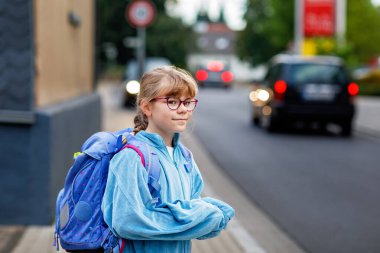 Gözlüklü ve sırt çantalı mutlu bir ilkokul öğrencisi okula giderken yolda yürüyor. Gülümseyen öğrenci okula, eğitime ve çocukluk yaşam tarzı konseptine hazır..