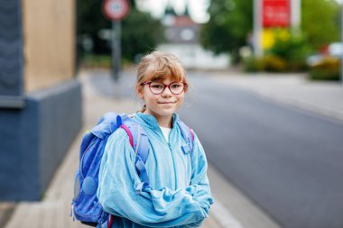 Gözlüklü ve sırt çantalı mutlu bir ilkokul öğrencisi okula giderken yolda yürüyor. Gülümseyen öğrenci okula, eğitime ve çocukluk yaşam tarzı konseptine hazır..
