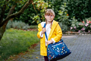 Gözlüklü ve sırt çantalı mutlu bir ilkokul öğrencisi okula giderken yolda yürüyor. Gülümseyen öğrenci okula, eğitime ve çocukluk yaşam tarzı konseptine hazır..