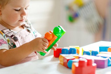 Çocuk odasında ya da evde eğitici oyuncakları olan sevimli bir kız. Mutlu sağlıklı çocuk farklı renkli plastik bloklarla eğleniyor. Sevimli bebek öğrenimi yaratma.