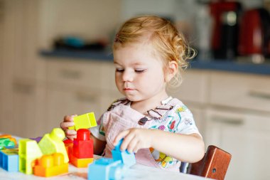 Çocuk odasında ya da evde eğitici oyuncakları olan sevimli bir kız. Mutlu sağlıklı çocuk farklı renkli plastik bloklarla eğleniyor. Sevimli bebek öğrenimi yaratma.