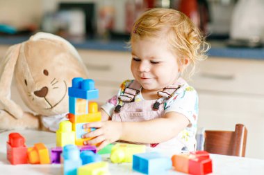 Bebek odasında eğitici oyuncaklarla oynayan pelüş tavşanlı sevimli bir kız. Mutlu sağlıklı çocuk evde renkli farklı plastik bloklarla eğleniyor. Sevimli bebek öğrenimi yaratma