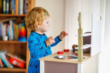 Oyuncak mutfağıyla oynayan sevimli küçük bir kız. Mutlu sağlıklı bir bebek. Rol yapma oyunuyla eğleniyor, evde veya çocuk odasında çömlek çaydanlığıyla oynuyor. Oyuncağı olan aktif bir çocuk