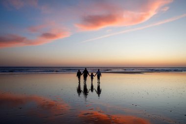 Gün batımında anneleriyle sahilde mutlu üç çocuk ve anne siluetinin portresi. Mutlu aile, kadın, iki okul çocuğu ve küçük bir anaokulu kızı. Kardeşler birlikte eğleniyor. Bağlanma.