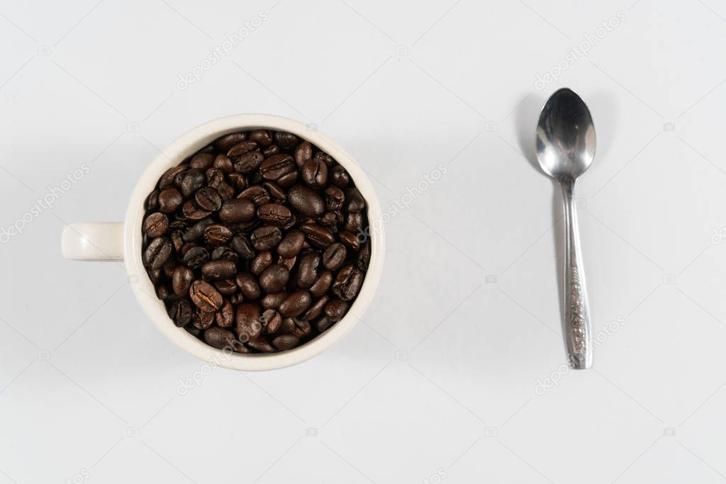 Coffee beans in white cup and spoon with white background