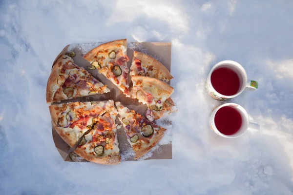 Kış pikniği: Bir dilim pizza ve karda iki fincan çay.