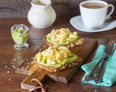Çırpılmış yumurta ve bir ahşap tahta üzerinde avokado püresi ile tost. Kahvaltı konsepti.