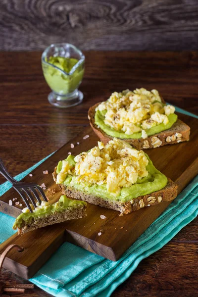 Toasts with scrambled egg and avocado puree on a wooden board. Breakfast concept.