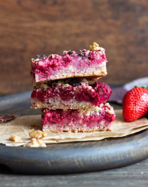 Kek veya çilek, çikolata ve cevizli tatlı ekmek kırıntısı (streusel) bir parşömen kağıt üzerinde seçici odak ile tatlılar yığını. Çilek barlar. Kare şekli. Geleneksel tatlar karışımı