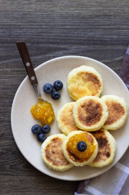Süzme peynir (syrniki) ekşi krema, Portakal Reçeli ve bir plaka üzerinde taze yaban mersini gözlemesi. Kahvaltı ve öğle yemeği kavramı. 