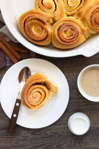 Cinnamon buns on a white plate and in a white ceramic form and cinnamon sticks