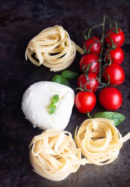 Makarna malzemeler. Kiraz domates, tagliatelle İtalyan Makarna, fesleğen ve mozzarella peyniri karanlık grunge zemin, kopya alanı, üstten görünüm üzerinde. Düz yatıyordu.