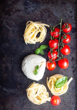 Makarna malzemeler. Kiraz domates, tagliatelle İtalyan Makarna, fesleğen ve mozzarella peyniri karanlık grunge zemin, kopya alanı, üstten görünüm üzerinde. Düz yatıyordu.