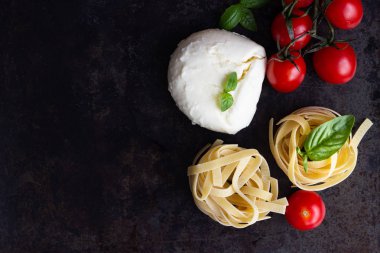 Makarna malzemeler. Kiraz domates, tagliatelle İtalyan Makarna, fesleğen ve mozzarella peyniri karanlık grunge zemin, kopya alanı, üstten görünüm üzerinde. Düz yatıyordu.