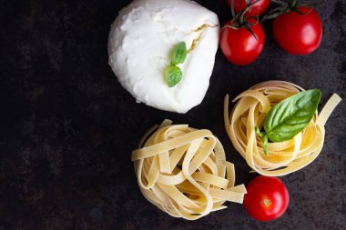 Makarna malzemeler. Kiraz domates, tagliatelle İtalyan Makarna, fesleğen ve mozzarella peyniri karanlık grunge zemin, kopya alanı, üstten görünüm üzerinde. Düz yatıyordu.