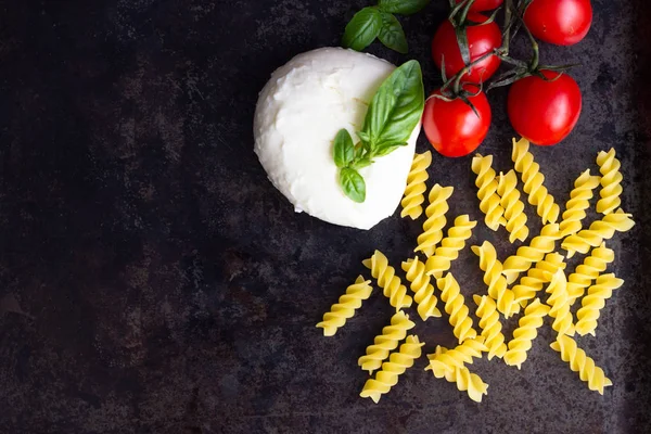 Makarna malzemeler. Kiraz domates, Düdük makarna çeşitleri, fesleğen, karanlık grunge zemin, kopya alanı, üstten görünüm üzerinde mozzarella peyniri. Düz yatıyordu.