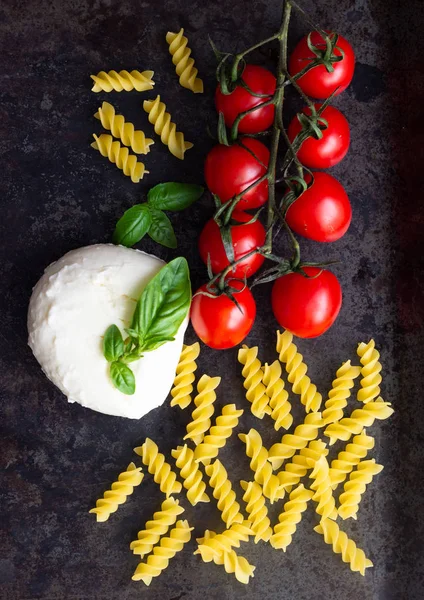 Makarna malzemeler. Kiraz domates, Düdük makarna çeşitleri, fesleğen, karanlık grunge zemin, kopya alanı, üstten görünüm üzerinde mozzarella peyniri. Düz yatıyordu.