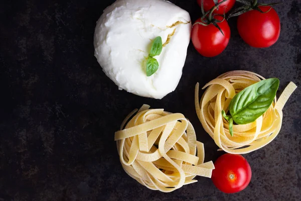 Makarna malzemeler. Kiraz domates, tagliatelle İtalyan Makarna, fesleğen ve mozzarella peyniri karanlık grunge zemin, kopya alanı, üstten görünüm üzerinde. Düz yatıyordu.