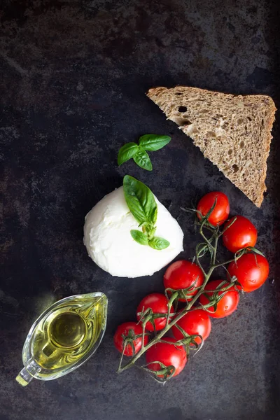 Fresh basil, mozzarella cheese, olive oil and cherry tomatoes on dark background. Italian food or ingredients background. Caprese. Copy space, top view.