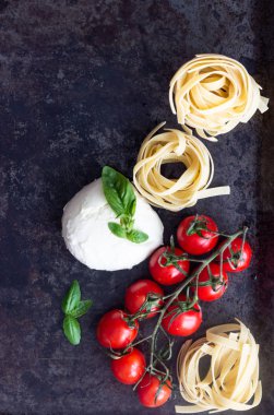 Makarna malzemeler. Kiraz domates, tagliatelle İtalyan Makarna, fesleğen ve mozzarella peyniri karanlık grunge zemin, kopya alanı, üstten görünüm üzerinde. Düz yatıyordu.