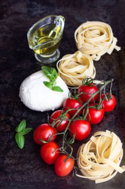 Makarna malzemeler. Kiraz domates, tagliatelle İtalyan Makarna, fesleğen, mozzarella peyniri ve Zeytinyağı karanlık grunge zemin, tarih alan, üstten görünüm kopyalayın. Düz yatıyordu.