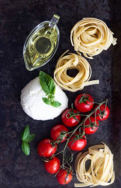 Makarna malzemeler. Kiraz domates, tagliatelle İtalyan Makarna, fesleğen, mozzarella peyniri ve Zeytinyağı karanlık grunge zemin, tarih alan, üstten görünüm kopyalayın. Düz yatıyordu.