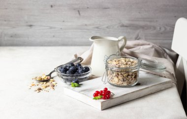 Ev yapımı granola açık cam kavanoz, süt, yaban mersini, frenk üzümü ve nane açık renkli, sağlıklı kahvaltı malzemeler üzerinde. Kopya alanı