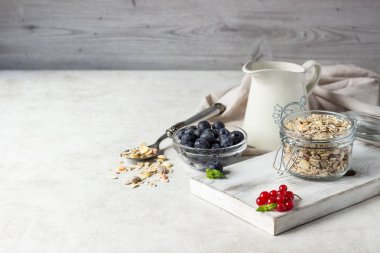Ev yapımı granola açık cam kavanoz, süt, yaban mersini, frenk üzümü ve nane açık renkli, sağlıklı kahvaltı malzemeler üzerinde. Kopya alanı