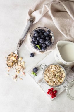Ev yapımı granola açık cam kavanoz, süt, yaban mersini, frenk üzümü ve nane açık renkli, sağlıklı kahvaltı malzemeler üzerinde. Kopya alanı