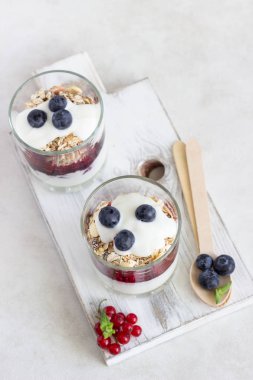 Çilek ve bir beyaz tahta üzerinde bardaklarda granola ev yapımı organik yoğurt parfe. Sağlıklı kahvaltı