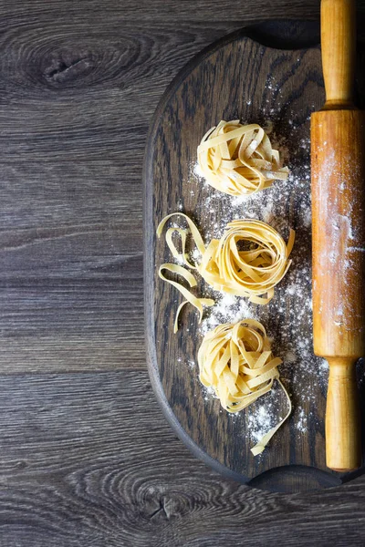 Ahşap kesme tahtası üzerinde ham tagliatelle makarna. El yapımı geleneksel makarna çeşitleri.