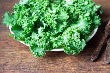 Kale. Ahşap arka plan üzerinde plaka üzerinde yeşil sebze yaprakları. Sağlıklı beslenme, vejetaryen yemek.