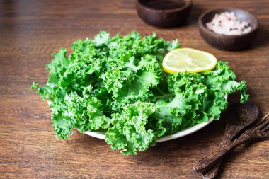 Kale. Ahşap arka plan üzerinde plaka üzerinde yeşil sebze yaprakları. Sağlıklı beslenme, vejetaryen yemek.