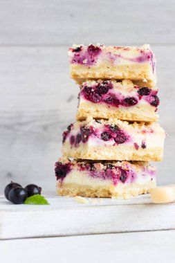 Siyah frenk üzümü kek. Limon, siyah frenk üzümü ve bir beyaz tahta kesme tahtası üzerinde streusel ile peynirli kek barlar.