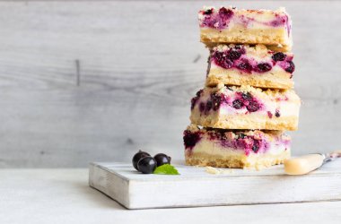 Siyah frenk üzümü kek. Limon, siyah frenk üzümü ve bir beyaz tahta kesme tahtası üzerinde streusel ile peynirli kek barlar.