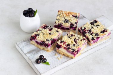 Siyah frenk üzümü kek. Limon, siyah frenk üzümü ve bir beyaz tahta kesme tahtası üzerinde streusel ile peynirli kek barlar.