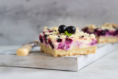 Siyah frenk üzümü kek. Limon, siyah frenk üzümü ve bir beyaz tahta kesme tahtası üzerinde streusel ile peynirli kek barlar.