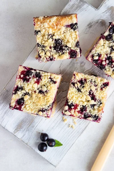 Siyah frenk üzümü kek. Limon, siyah frenk üzümü ve bir beyaz tahta kesme tahtası üzerinde streusel ile peynirli kek barlar.