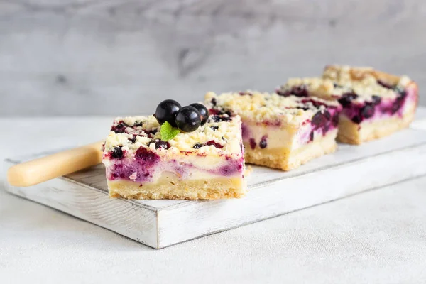 Siyah frenk üzümü kek. Limon, siyah frenk üzümü ve bir beyaz tahta kesme tahtası üzerinde streusel ile peynirli kek barlar.