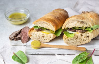 Beyaz ahşap kesme tahtası üzerinde soğan ve cukes ve Hardal soslu etli sandviç taze salata, kızartma