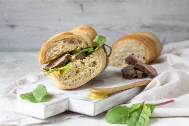 Beyaz ahşap kesme tahtası üzerinde soğan ve cukes ve Hardal soslu etli sandviç taze salata, kızartma